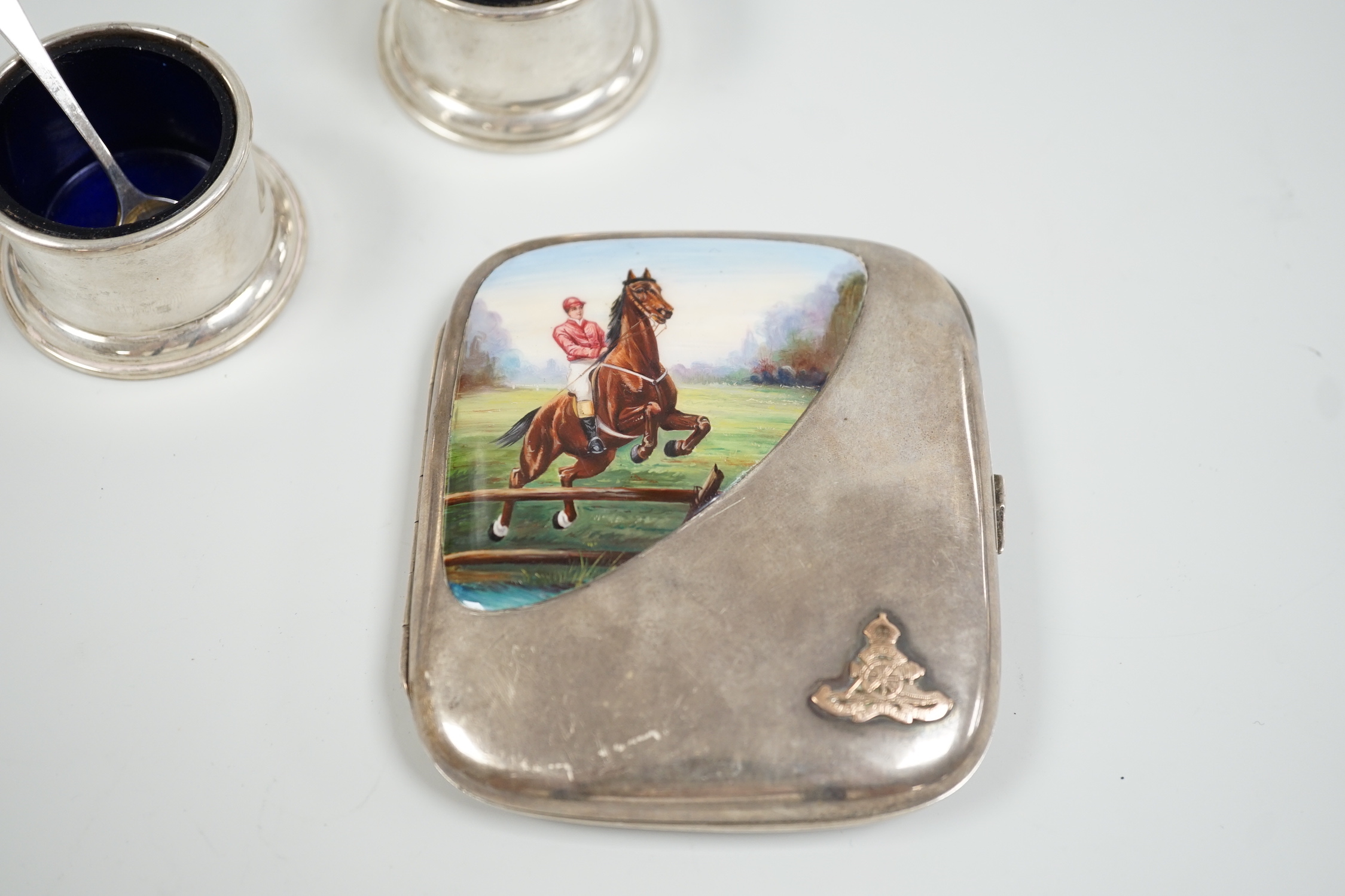 An Edwardian silver and enamel cigarette case, decoration with horse and jockey leaping a fence, import marks for Birmingham, 1908, 96mm, with military applique and inscription and a pair of Birks sterling condiments.